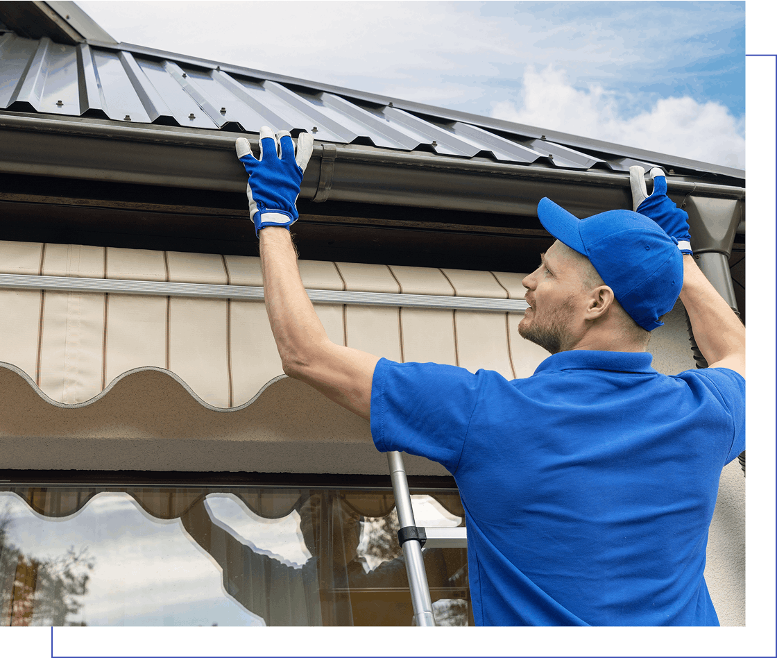 Person on ladder wearing blue uniform and gloves, inspecting a house gutter under a metal roof.