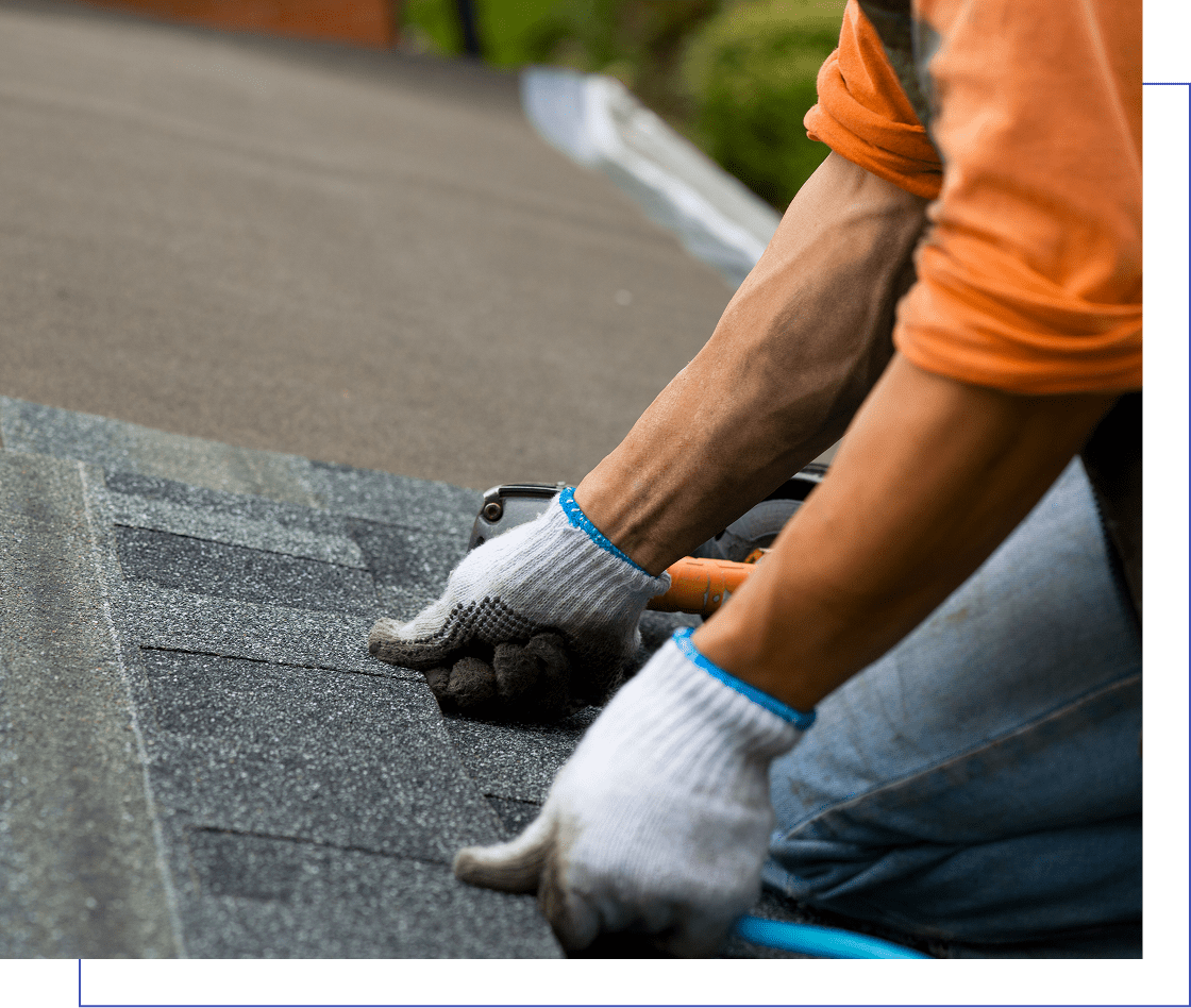 Person wearing gloves and orange shirt installing asphalt shingles on a roof.